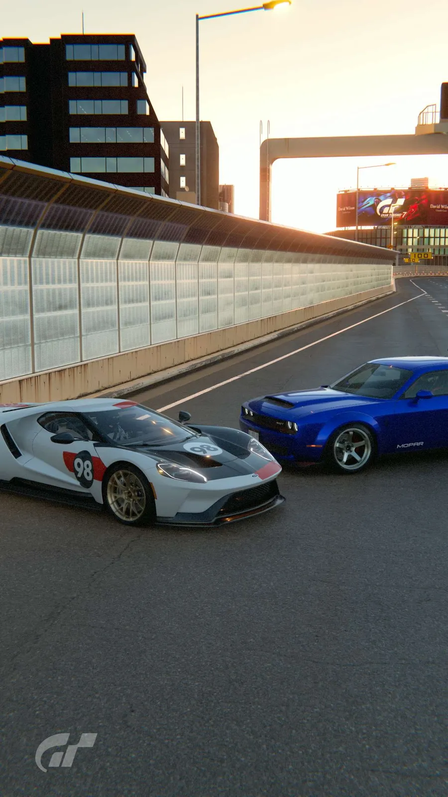 A white number 98 supercar and a blue muscle car parked on a city expressway at sunset